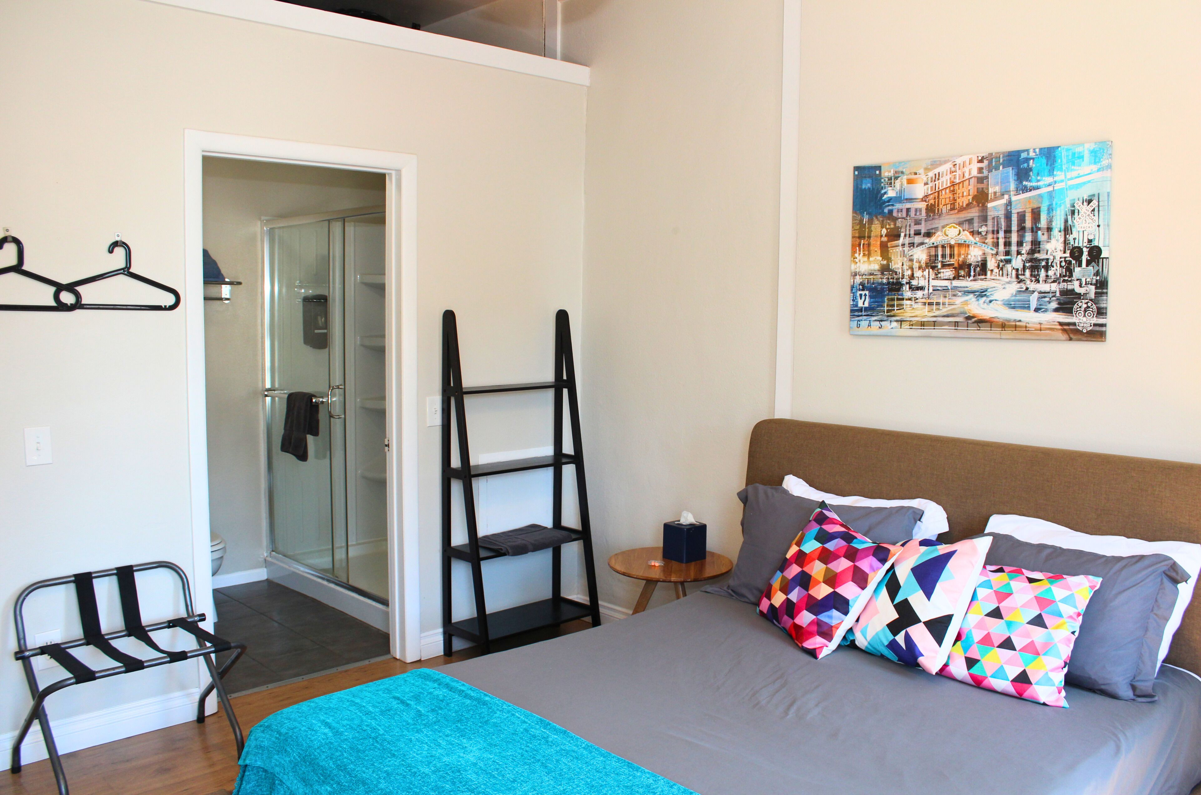A bedroom with a bed, pillows, a side table, a towel rack, and a painting on the wall.