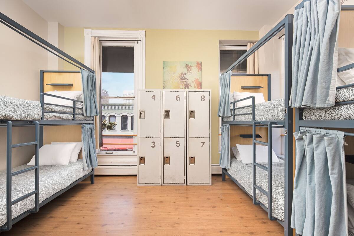Un dormitorio con literas, una serie de taquillas y vistas a un edificio a través de una puerta.