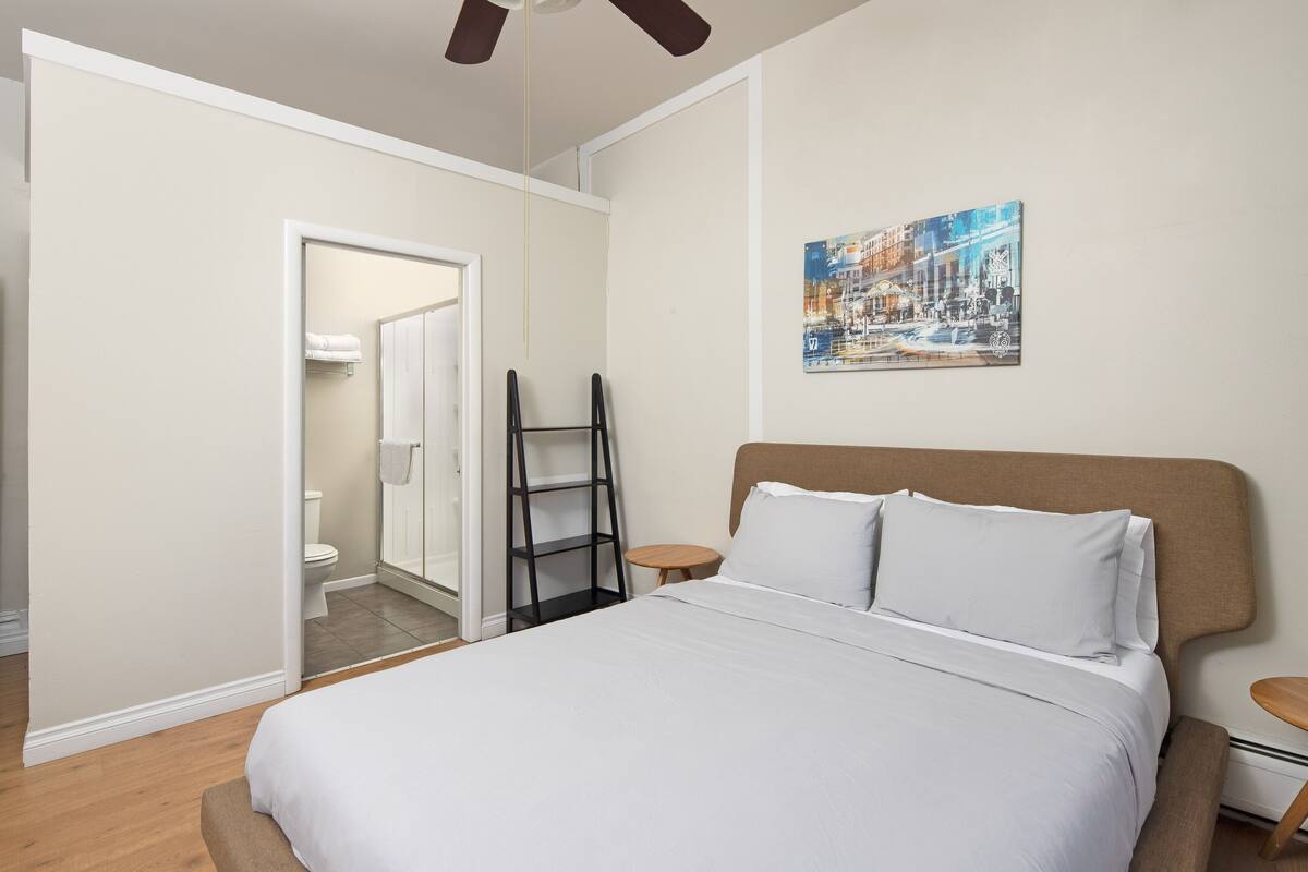 Un dormitorio con una cama, una mesita de noche, un estante en la pared y un cuadro.
