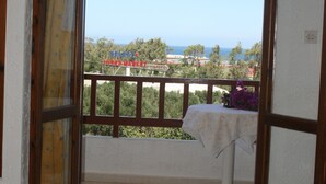 Un balcon avec vue sur la mer, une table recouverte d’une nappe et une serviette enroulée posée sur le sol.