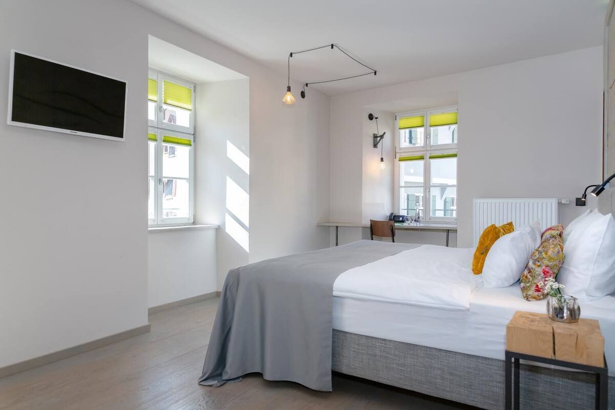 Una habitación de hotel moderna con una cama grande, un escritorio y dos ventanas con persianas.