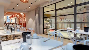 A modern dining area with white tables and chairs, a large window with artwork, and a chandelier.