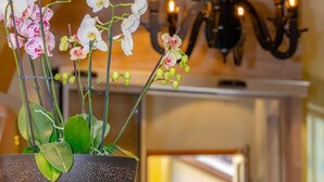 A black perforated bowl with white and pink orchids on a wooden pedestal in a well-lit hallway with a chandelier. - Hotel Luise & Luisenhof (Dinkelsbuehl)