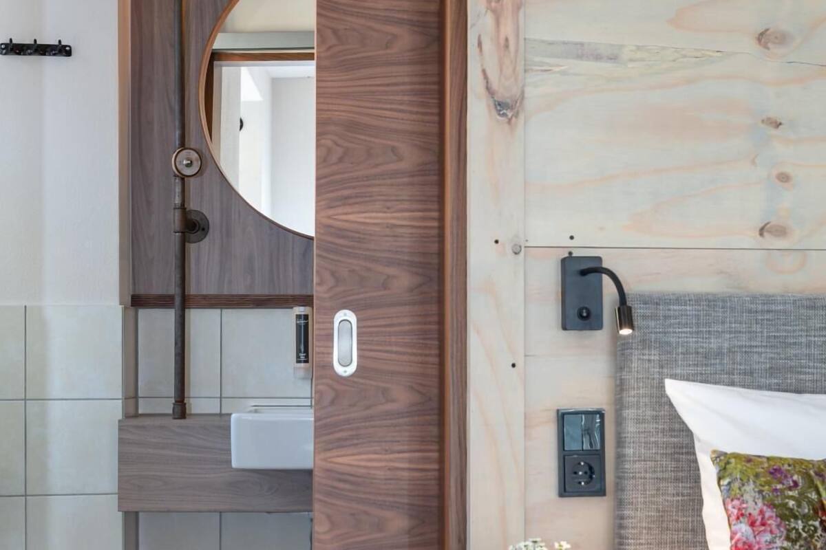 Un baño moderno con tocador de madera, espejo redondo y mesita de noche con lámpara.
