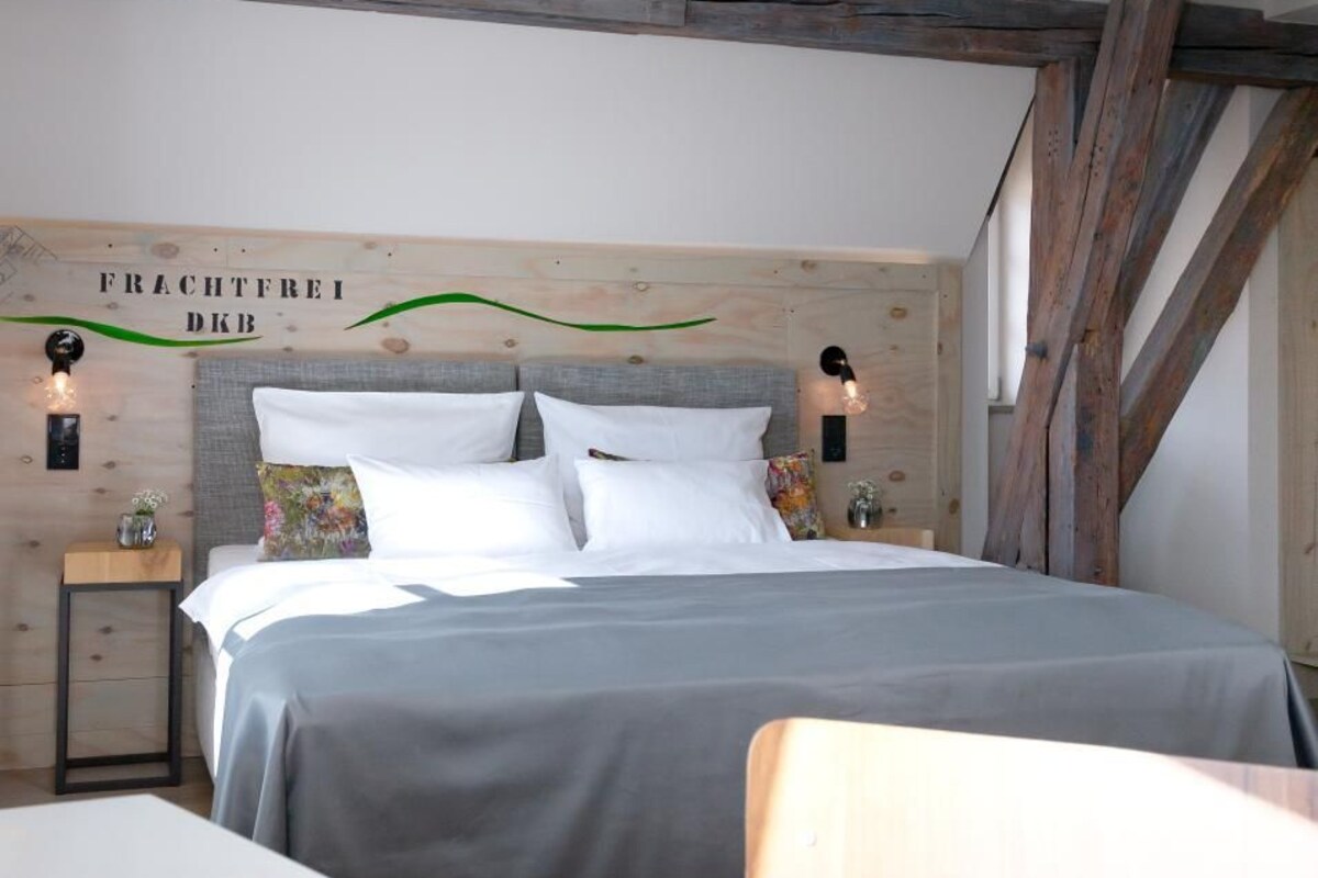 Une chambre à coucher comprenant un lit, des tables de chevet, une petite table, une table avec des verres et une tasse, et une poutre en bois au plafond.