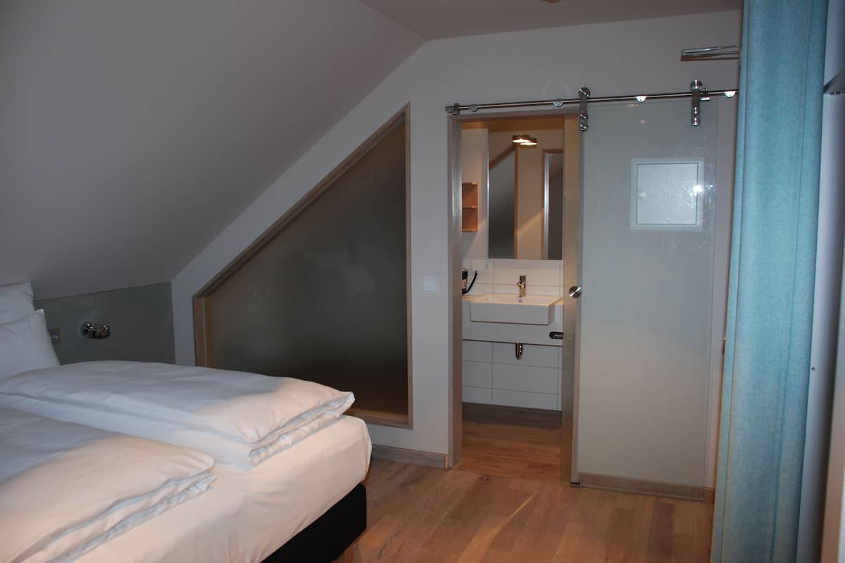 Un dormitorio con cama, un baño con espejo y lavamanos, y una puerta que da a otra habitación.