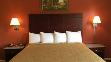 A hotel room with a large bed, two bedside tables, a painting on the wall, and two wall-mounted lamps.
