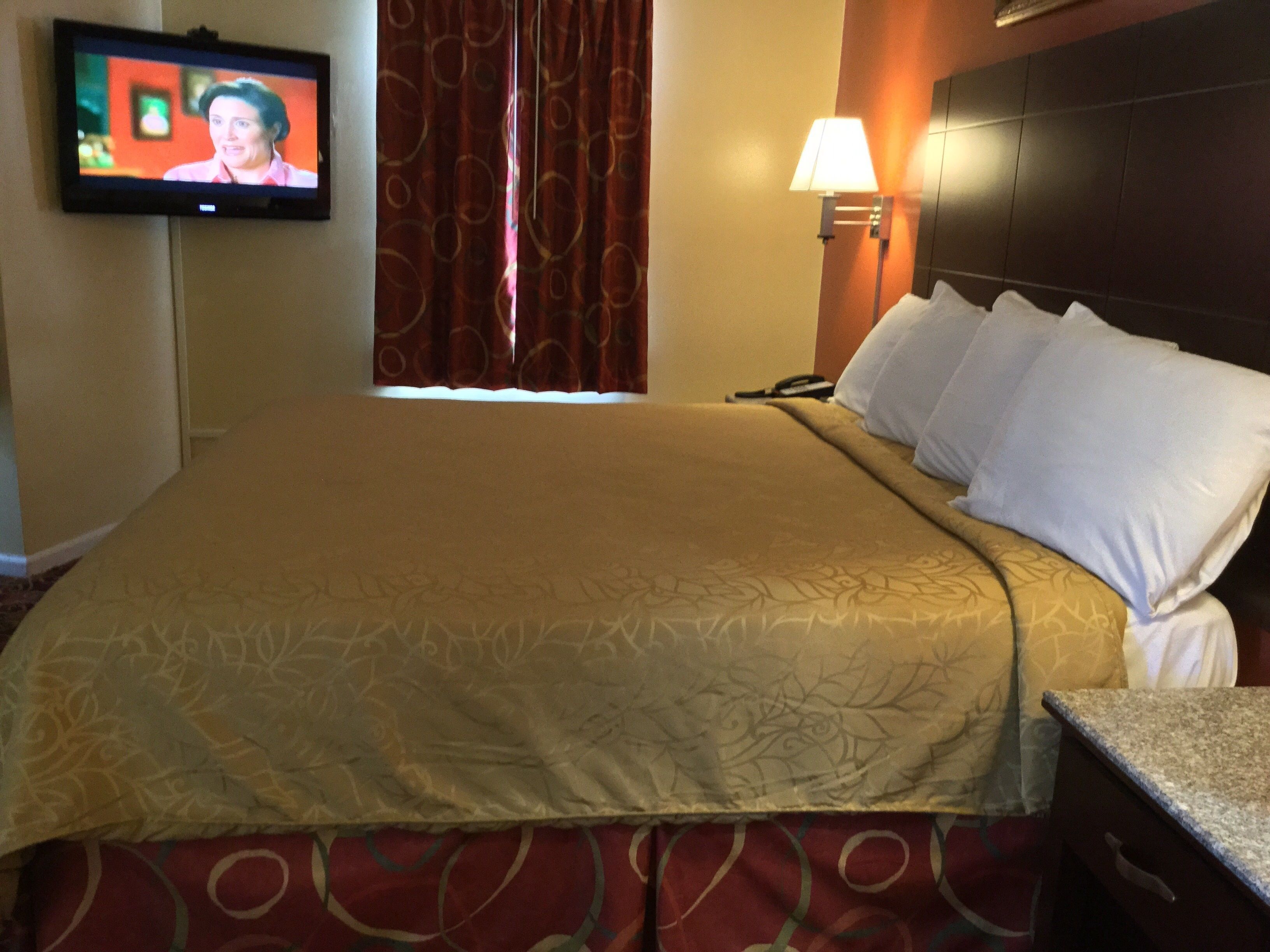 Habitación de hotel con una cama grande, un televisor montado en la pared, una lámpara de noche y un teléfono.