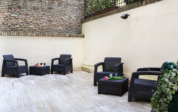 Un patio con mobiliario de mimbre, un muro de ladrillo y una pared blanca con una lámpara.