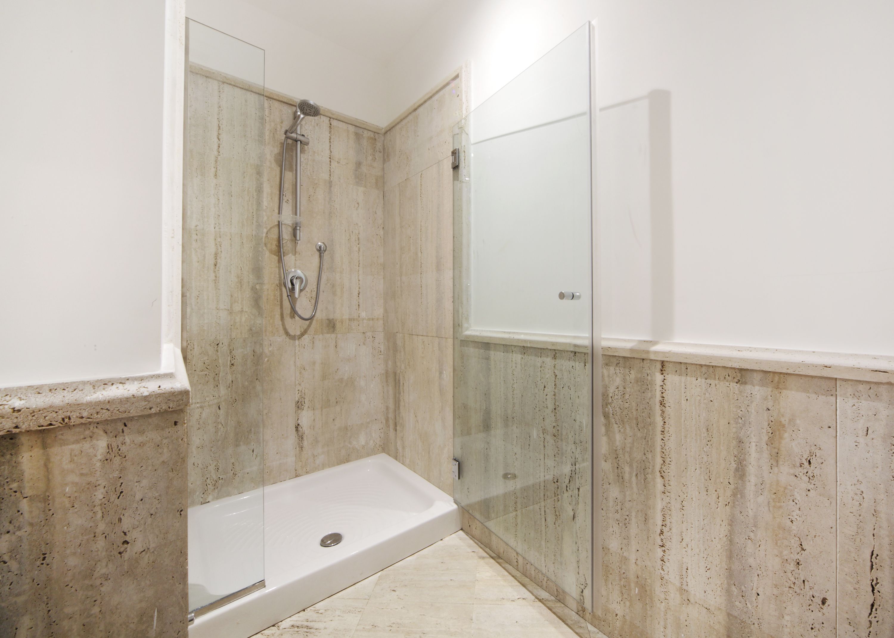 A shower area with a glass door, a showerhead, and a white bathtub.