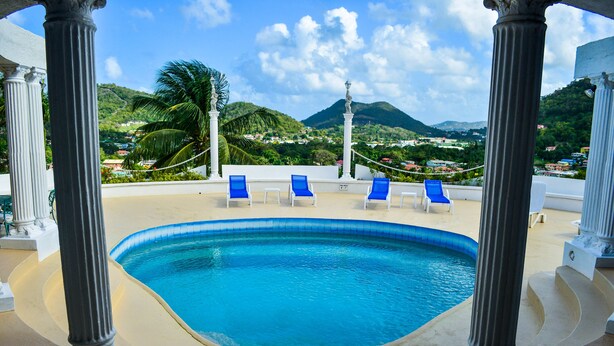 A swimming pool with blue water, surrounded by white columns, and blue lounge chairs.