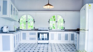 A kitchen with white cabinets, a black and white tiled floor, and two arched windows with greenery outside.