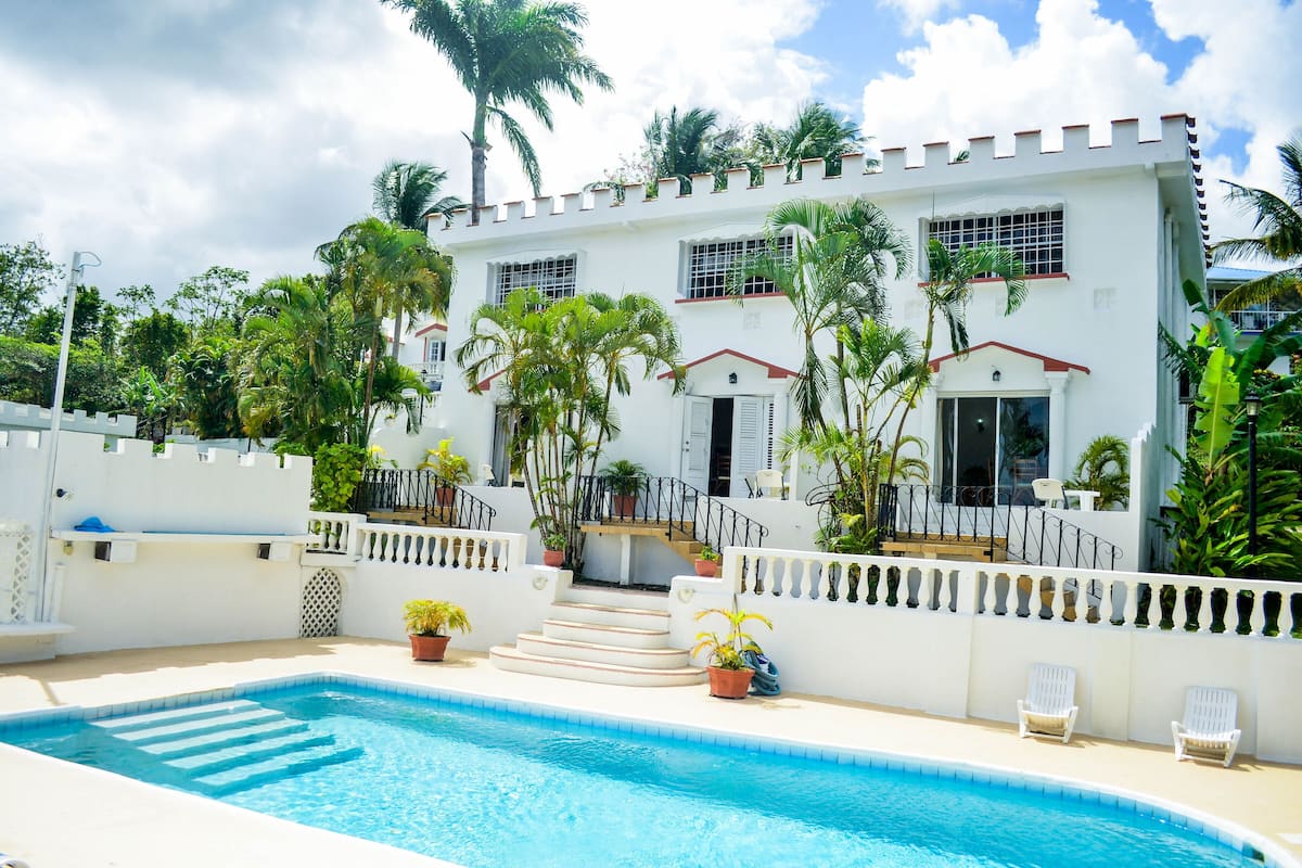 A white building with a pool, palm trees, and white chairs.
