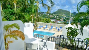 A balcony with a pool, white chairs, and a view of a town and mountains.