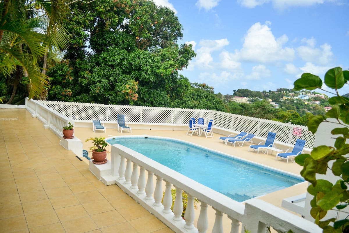 A swimming pool with a white balustrade, surrounded by blue lounge chairs and potted plants.