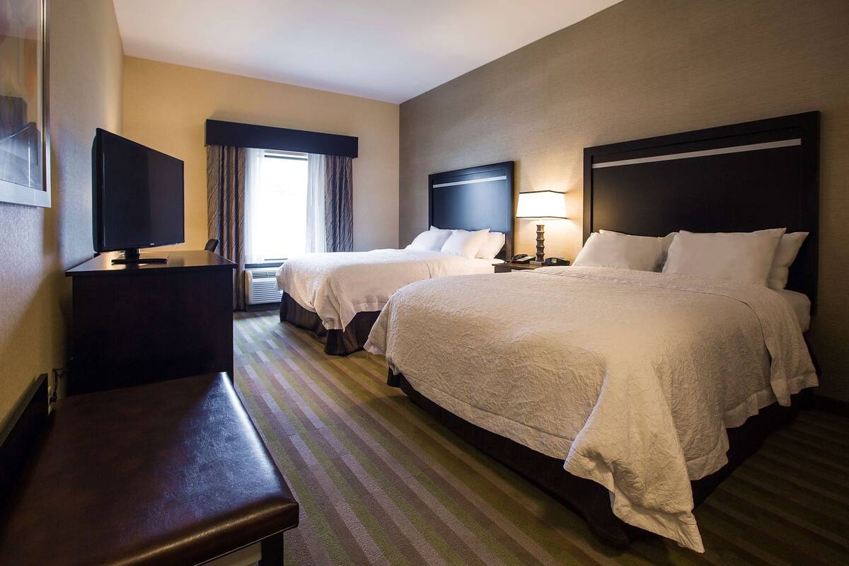 Quarto de hotel com duas camas, uma escrivaninha, televisão e abajur.
