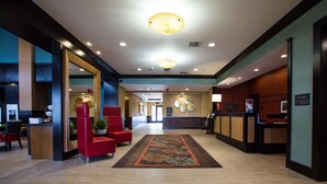 A hotel lobby with a reception desk, red seating area, and a decorative rug.