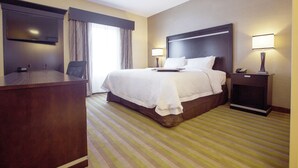 A hotel room with a large bed, a desk, a TV, and a nightstand with a lamp.