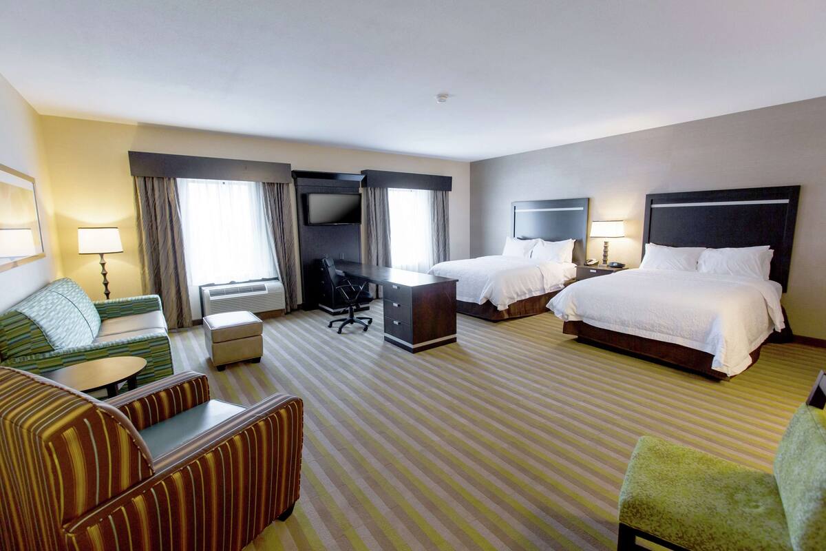 Quarto de hotel com duas camas, um sofá, uma mesa de escritório e uma televisão.