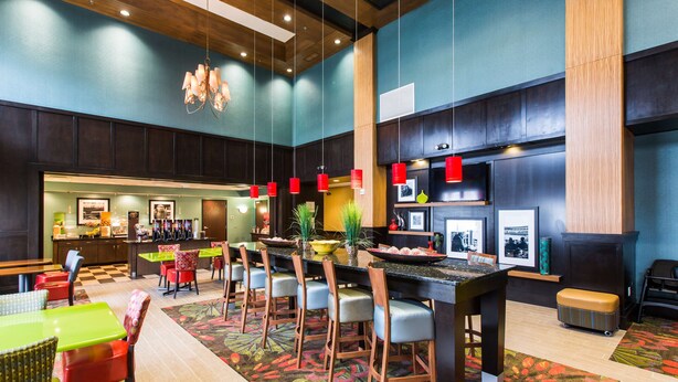 A spacious hotel lobby with a long reception desk, multiple seating areas, and a bar.