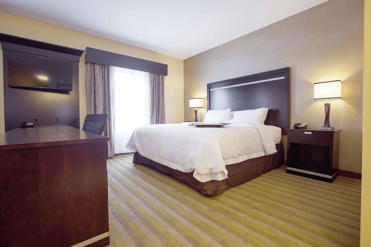 Una habitación de hotel con cama, escritorio, silla, televisor y mesita de noche con lámpara.
