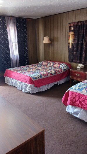 A room with two beds, a wooden floor, a lamp, a telephone, and a patterned curtain. - White Pine Motel (Ely)