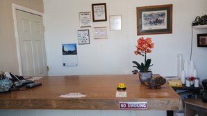 Un mostrador de recepción con un cartel de 'No Fumar', avisos enmarcados, un calendario y una planta en maceta.
