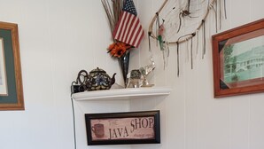 Una estación de café con un cartel que dice 'The Java Shop siempre abierto', una pequeña bandera estadounidense y un atrapasueños en la pared.