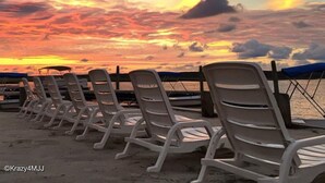 Een rij witte ligstoelen gericht op een zonsondergang boven het water.