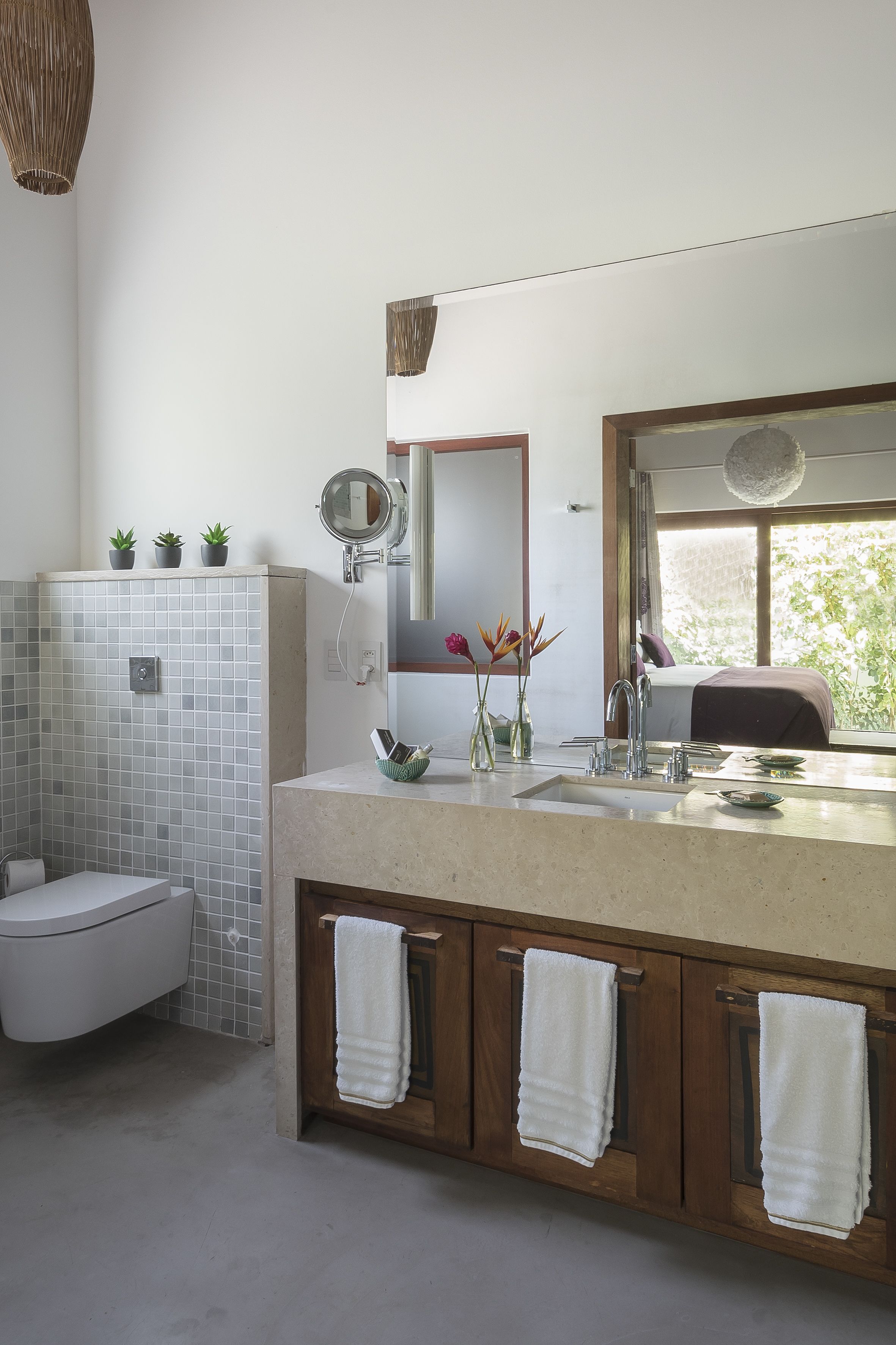 A modern bathroom with a white toilet, a sink with a mirror, and a window providing natural light.