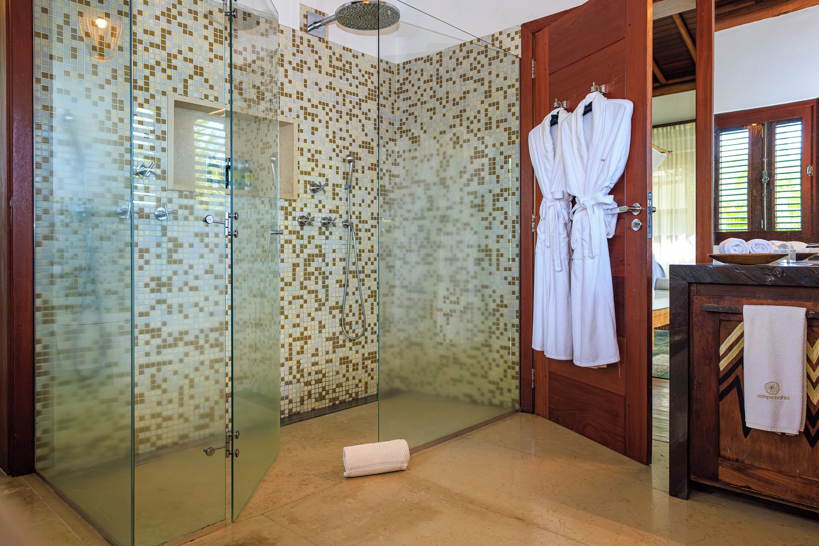 A glass-enclosed shower with mosaic tiles, a wooden door, and a towel on the floor.