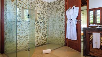 A glass-enclosed shower with mosaic tiles, a wooden door, and a towel on the floor.