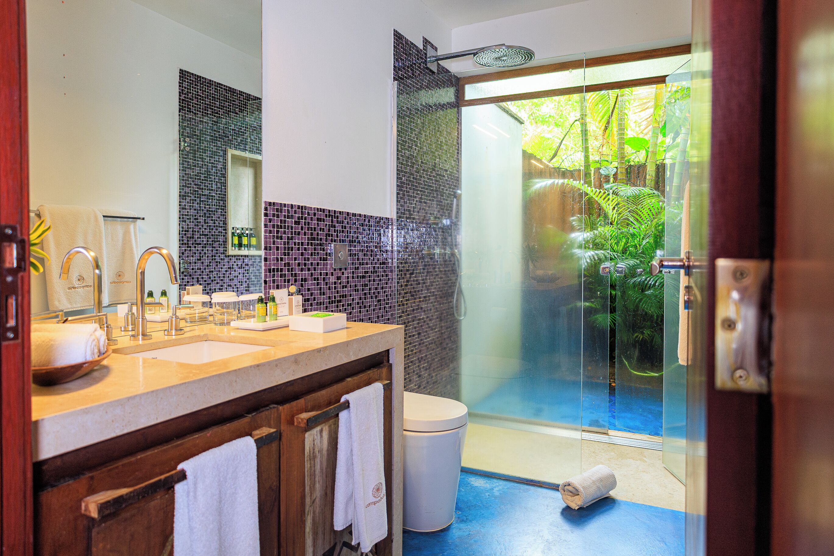 A bathroom with a glass shower, a sink with toiletries, and a towel rack.