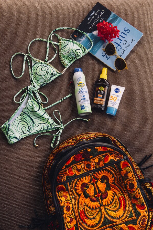A beach towel, a bikini, sunscreen, sunglasses, and a book on a brown surface.