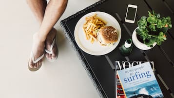 Uma bandeja com um hambúrguer e batatas fritas, um smartphone, uma revista e uma pequena planta sobre uma mesa.