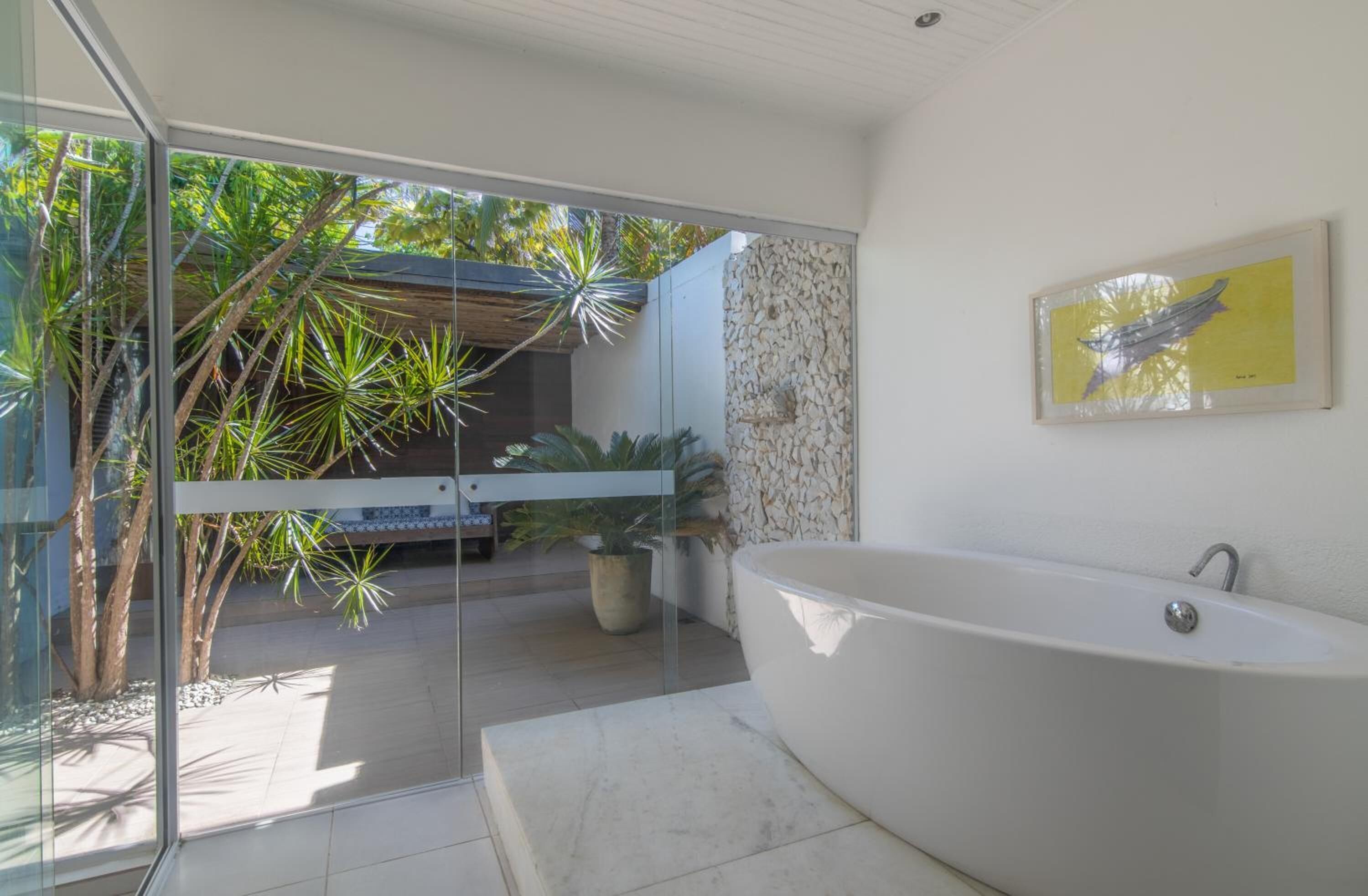 A modern bathroom with a freestanding bathtub, a glass shower enclosure, and a view of a tropical garden.