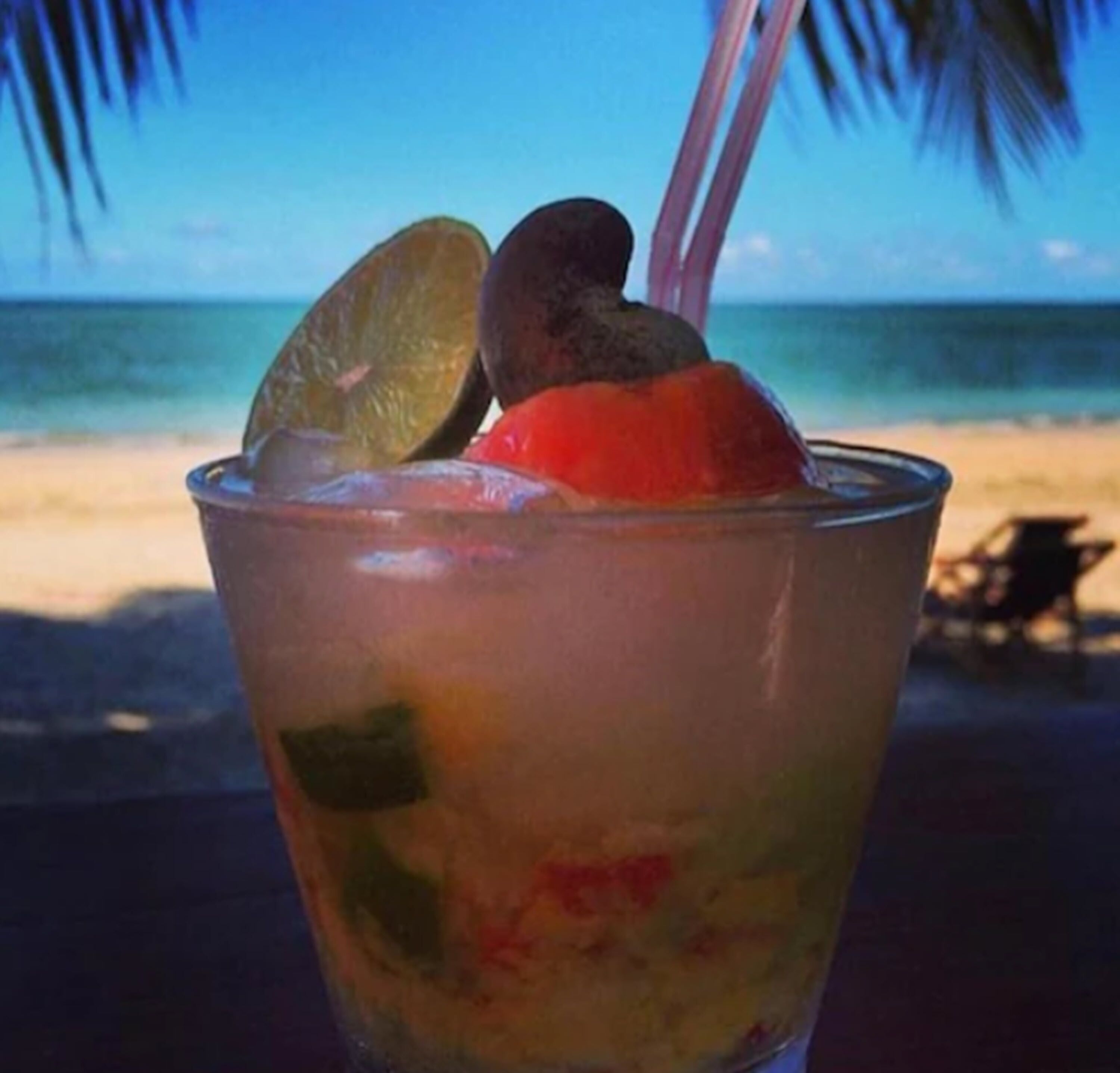 A tropical drink with lime and fruit, set against a beach backdrop.