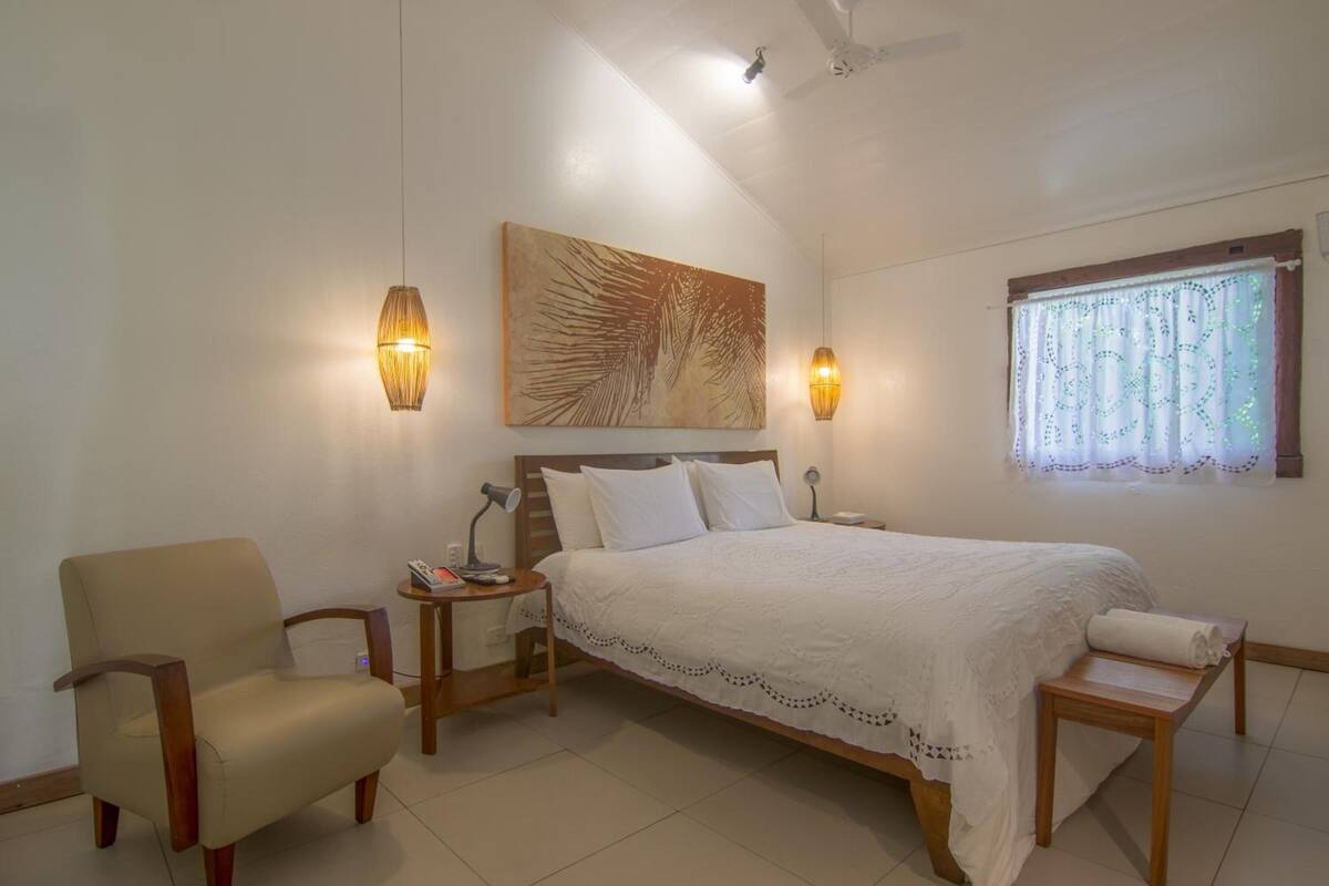 A bedroom with a bed, a chair, a bedside table, a lamp, and a painting on the wall.