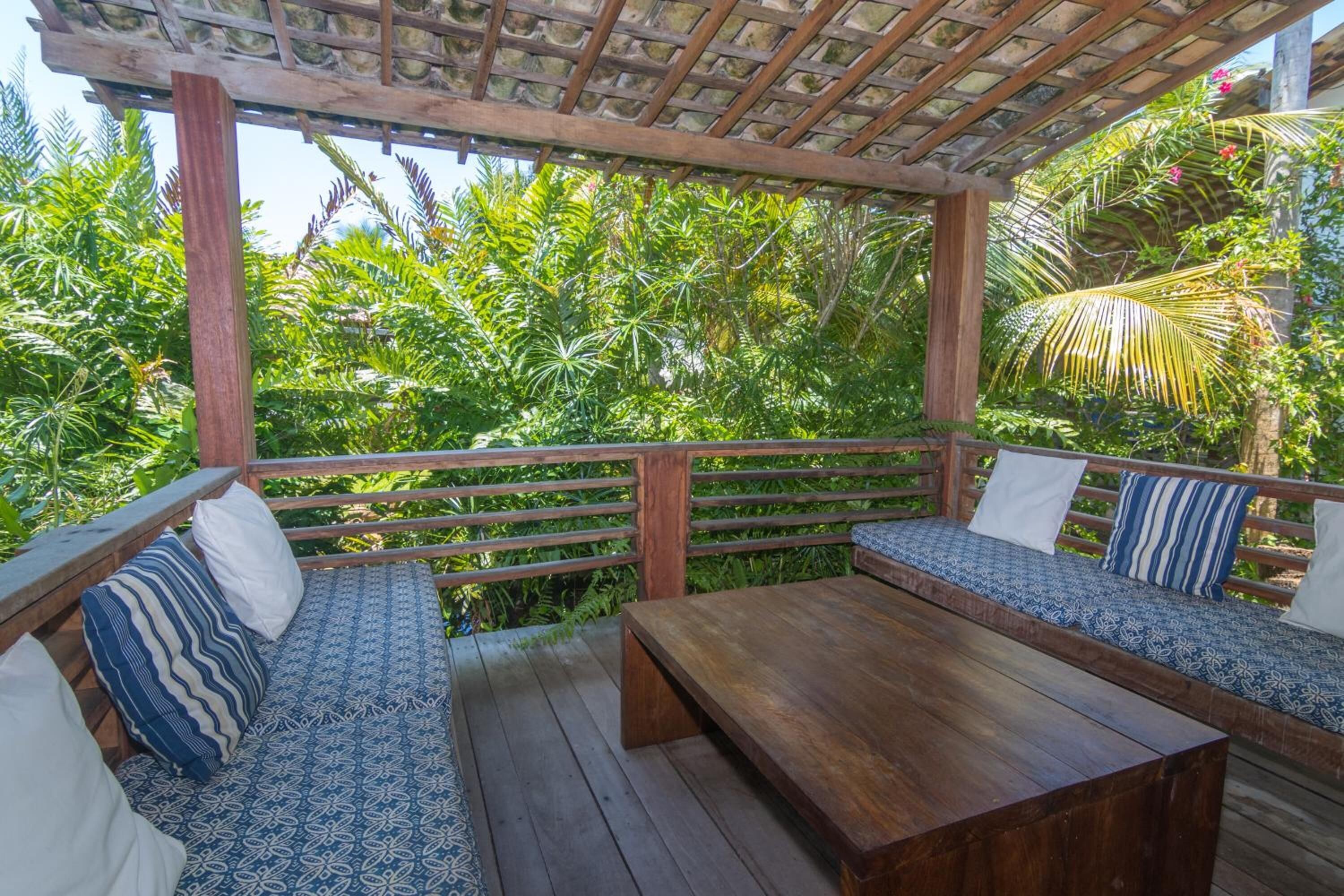 A wooden deck with a bench and a table, surrounded by lush greenery.
