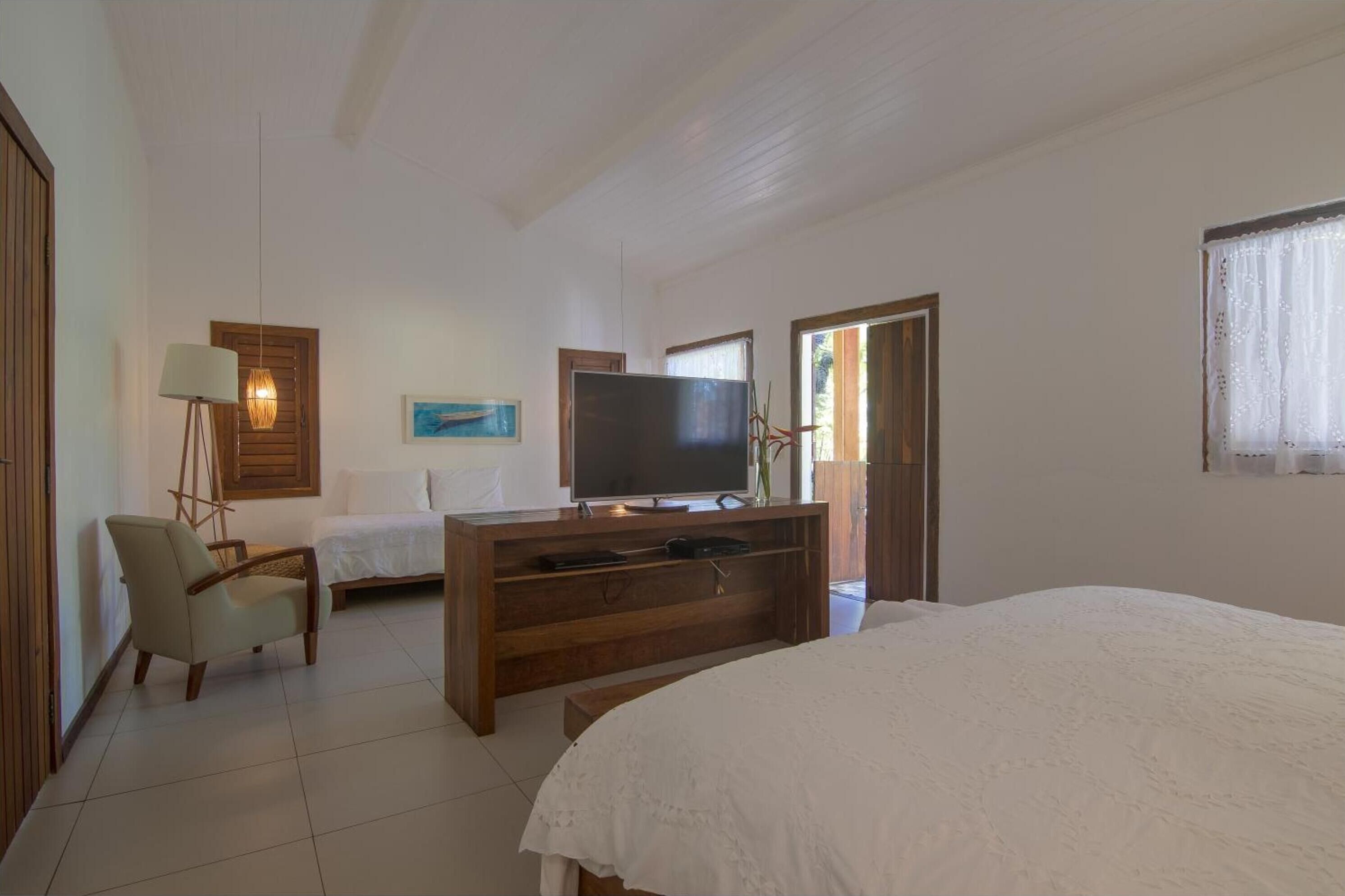 Quarto com cama, televisão sobre suporte de madeira, uma cadeira e uma escrivaninha.