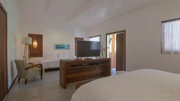 Quarto com cama, televisão sobre suporte de madeira, uma cadeira e uma escrivaninha.
