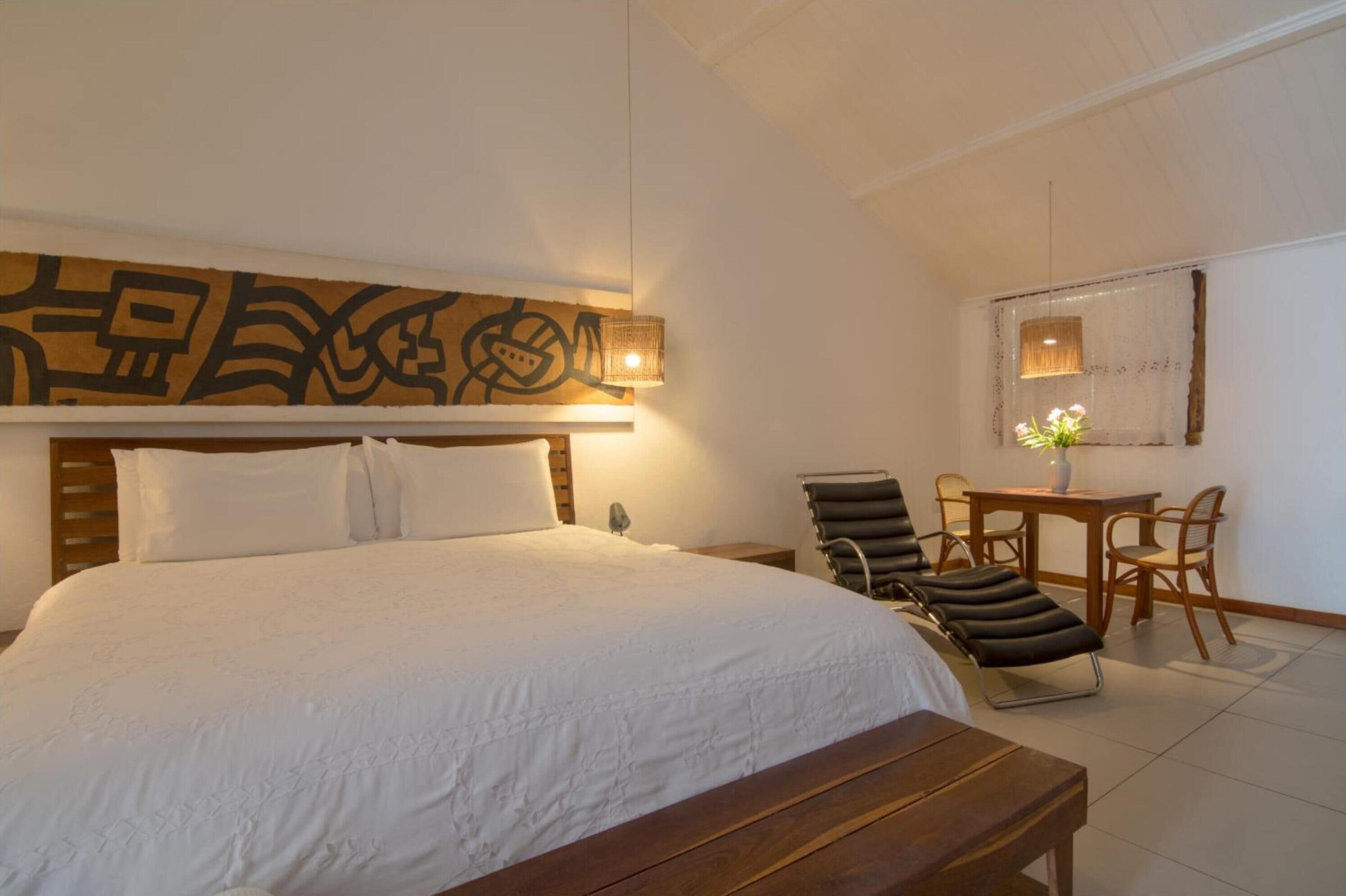 A hotel room with a large bed, a wooden headboard, a desk with chairs, and a wall-mounted artwork.