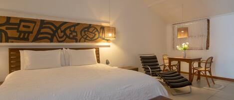 A hotel room with a large bed, a wooden headboard, a desk with chairs, and a wall-mounted artwork.