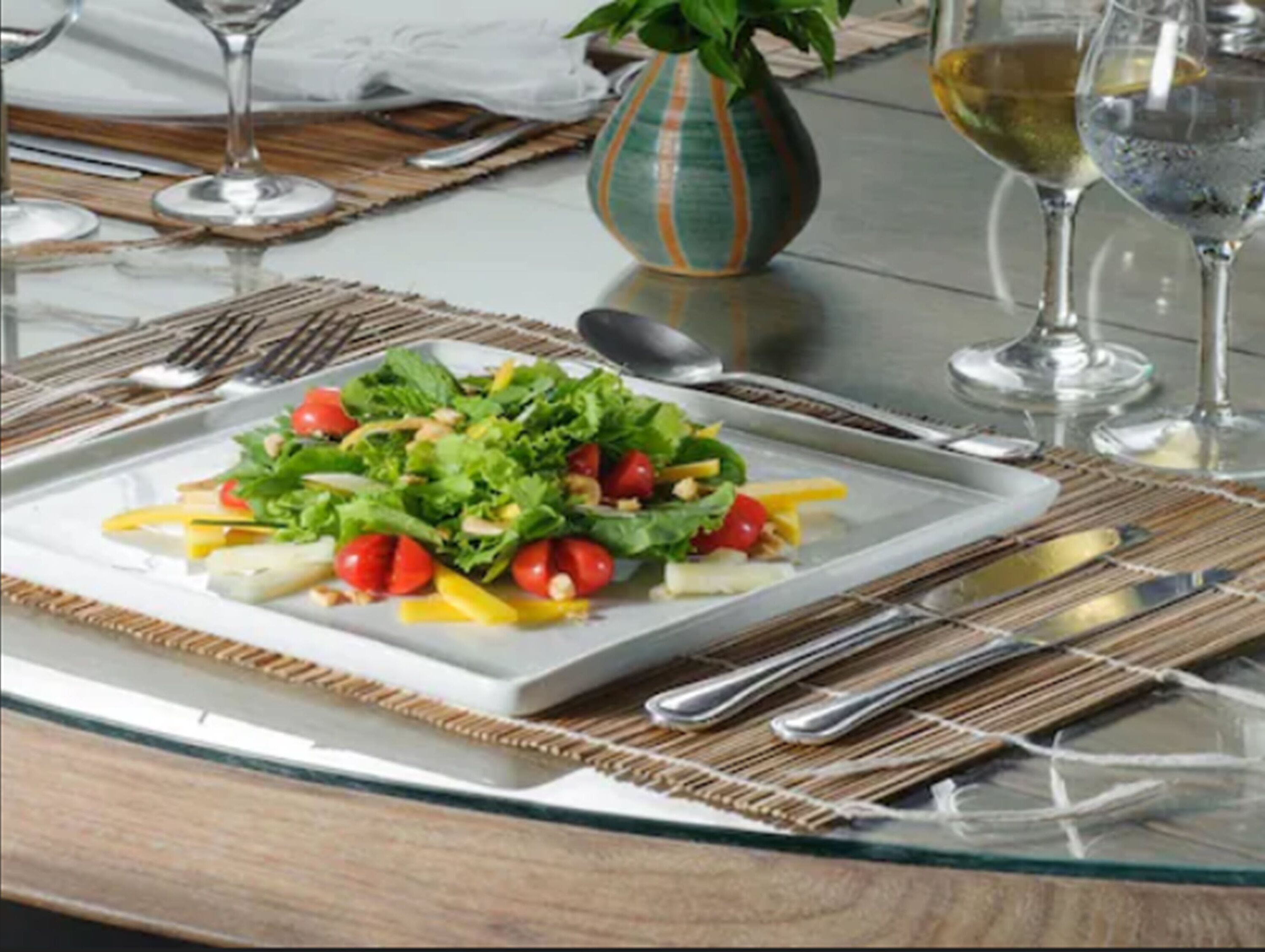 A table set with a salad, wine glasses, and cutlery.