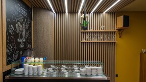 Una barra de desayuno con un menú en pizarra, una planta y una vitrina de vidrio con platos y aderezos.
