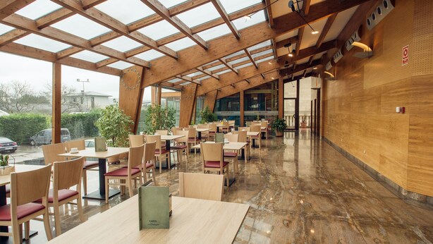 Un comedor amplio con mesas y sillas de madera, ventanas grandes y suelo pulido.