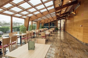 Un comedor amplio con mesas y sillas de madera, ventanas grandes y suelo pulido.
