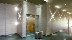 Un moderno vestíbulo de hotel con un ascensor de vidrio, una recepción y dos maletas en el suelo.