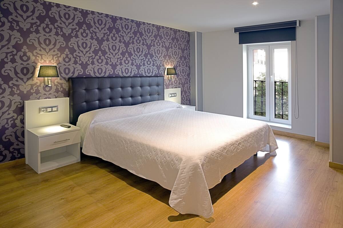 A bedroom with a large bed, two bedside lamps, a nightstand, and a window with a view.