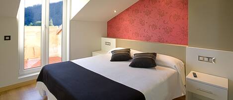A bedroom with a large bed, a nightstand, a bedside table, and a window with a view of a garden.